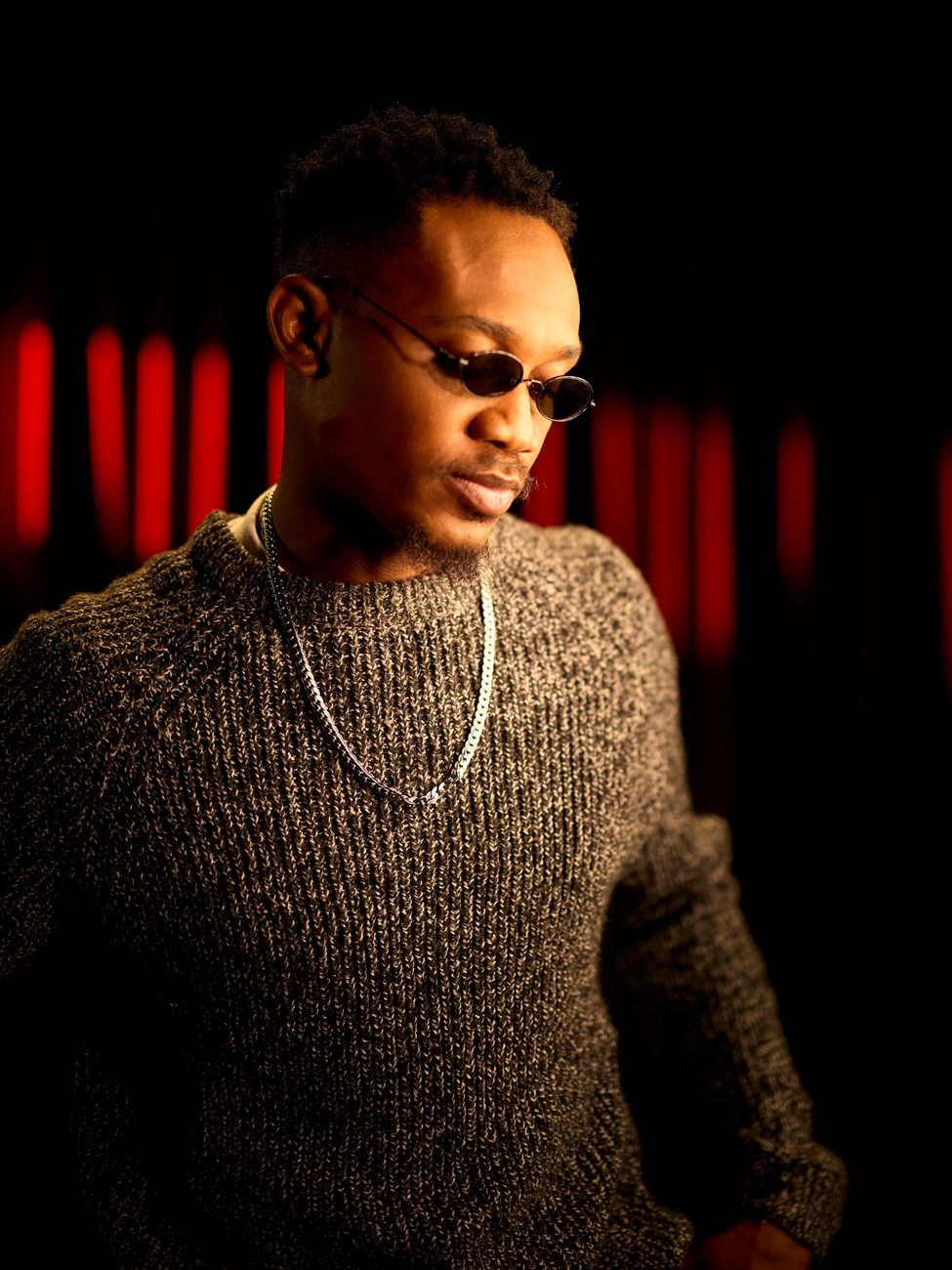 Sunkanmi Stephens in sunglasses and a knitted jumper, looking down